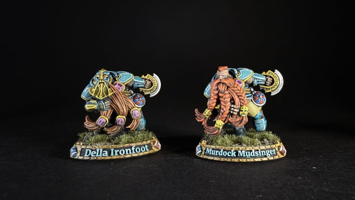 Two colorful fantasy dwarf miniatures on grassy bases, facing opposite directions, with name banners reading 'Della Ironfoot' and 'Murdock Mudsinger' (or similar).