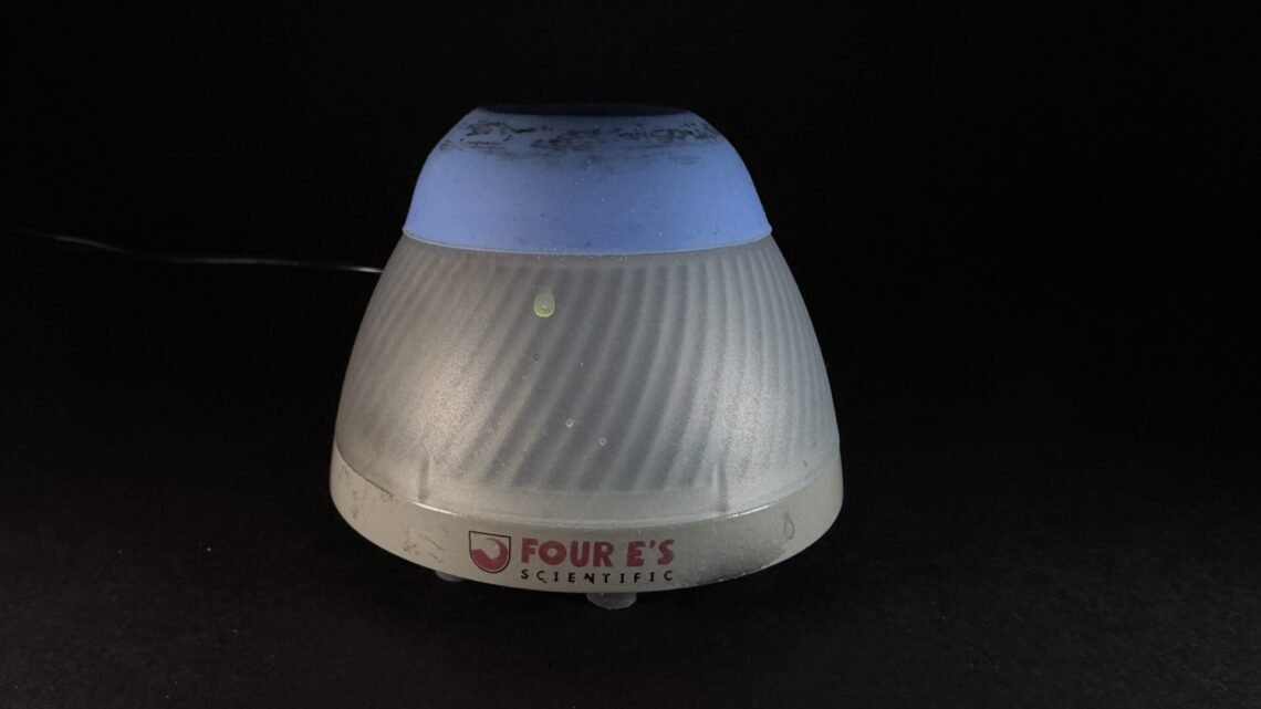 Cone-shaped, ribbed lamp with a blue top and gray base on a dark surface; brand reads 'FOUR'S SCIENTIFIC'.